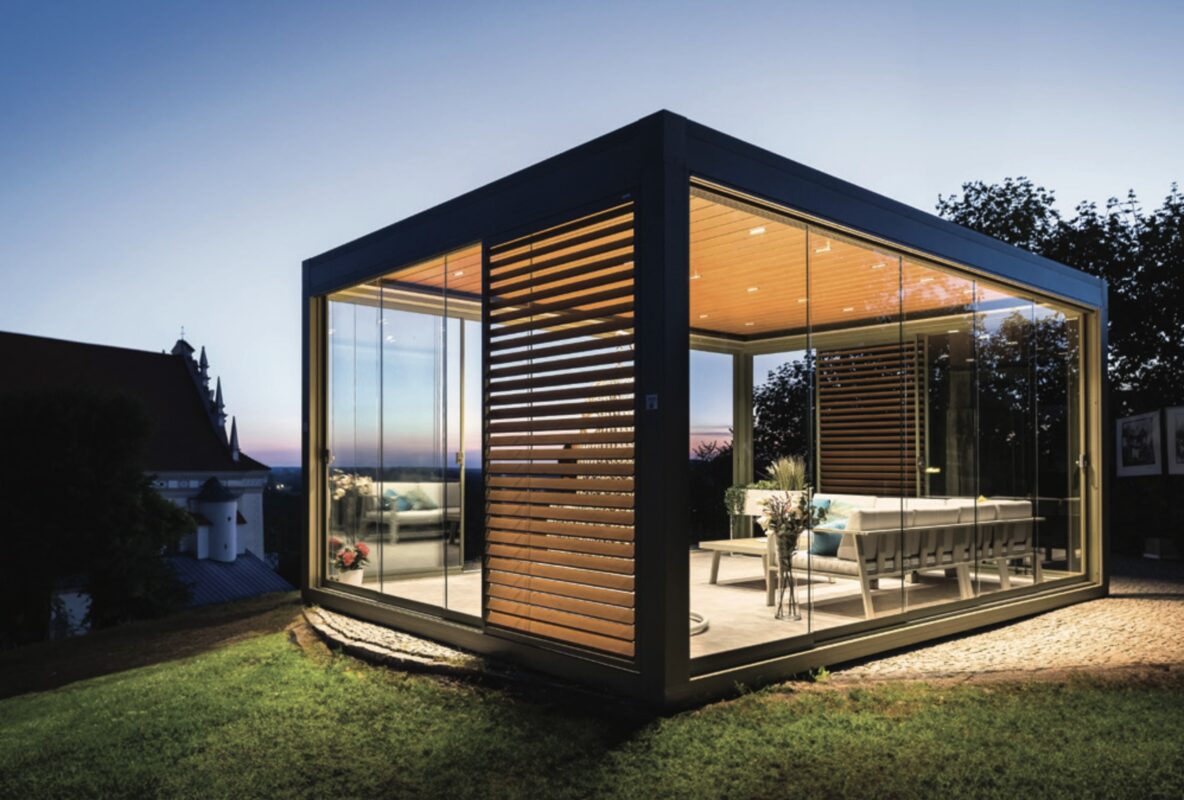 Beleuchteter, freistehender Kaltwintergarten aus Aluminium mit rahmenlosen Glas-Schiebeelementen als modernes Gartenzimmer.