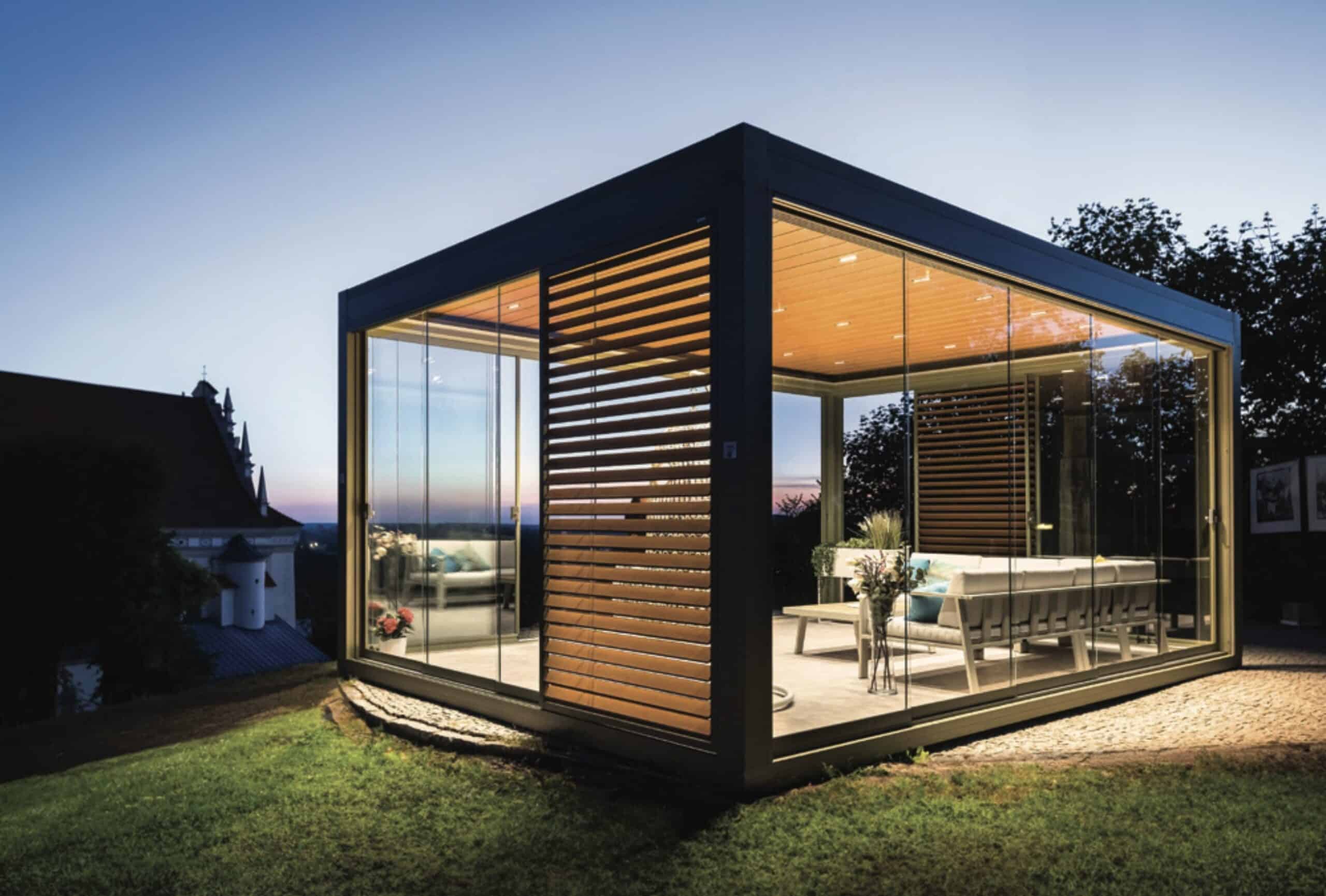 Beleuchteter, freistehender Kaltwintergarten aus Aluminium mit rahmenlosen Glas-Schiebeelementen als modernes Gartenzimmer.