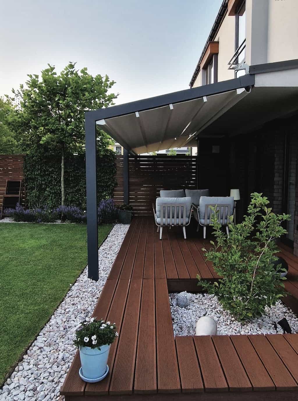 Elegante Aluminium-Terrassenüberdachung mit eingefahrenem Faltdach auf einer modernen Holzterrasse, umgeben von einem gepflegten Garten, zeigt wohnliches Ambiente im Freien.