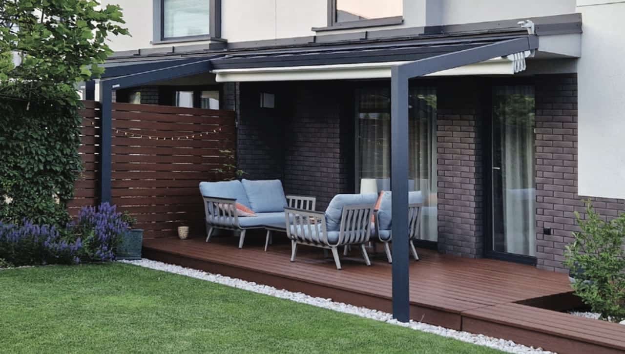 Moderne Terrassenüberdachung aus Aluminium als Pergola mit teilweise ausgefahrener, heller Faltmarkise, die flexiblen Sonnenschutz auf einer Holzterrasse bietet.