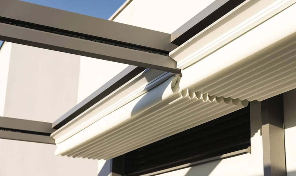Detailansicht einer modernen Pergola-Markise aus Aluminium mit eingefahrenem, wetterfestem Stoffdach unter einer Schutzabdeckung.