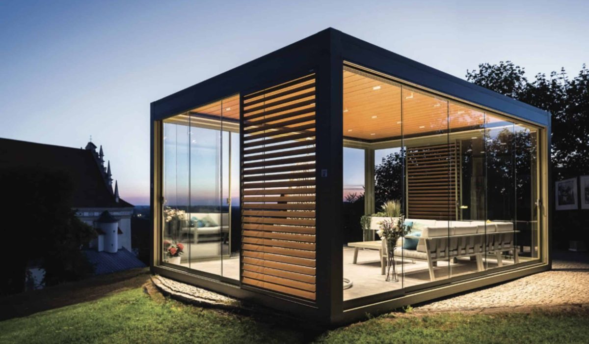 Beleuchteter, freistehender Kaltwintergarten aus Aluminium mit rahmenlosen Glas-Schiebeelementen als modernes Gartenzimmer.